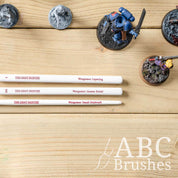 Close up of the handles of the Army Painters Most Wanted brush set, on a wooden surface and next to various mini figures. 