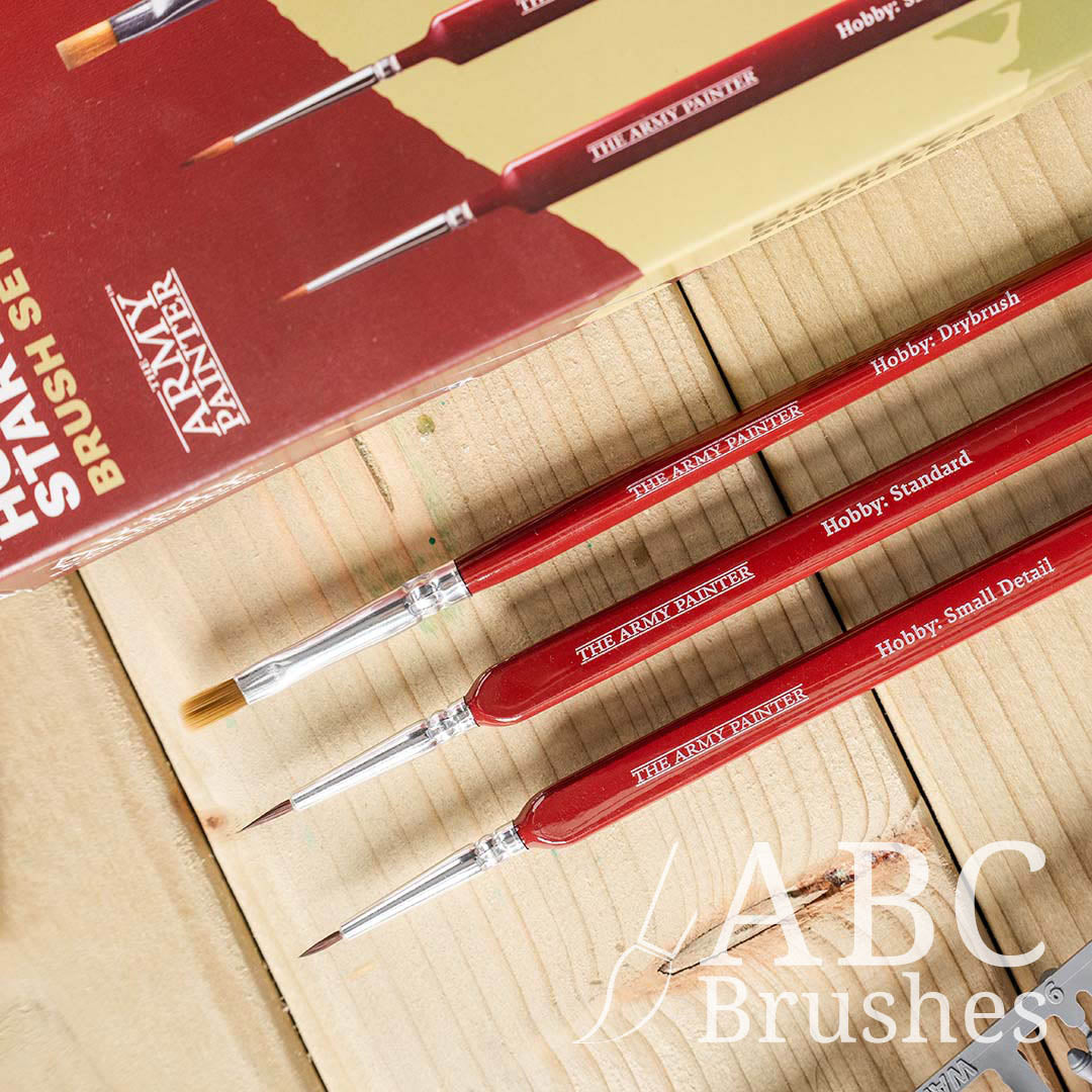 The Army Painter Hobby Starter brush set, laid out diagonally, next to the packaging on a wooden background.