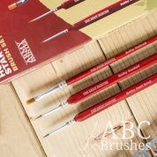 The Army Painter Hobby Starter brush set, laid out diagonally, next to the packaging on a wooden background.