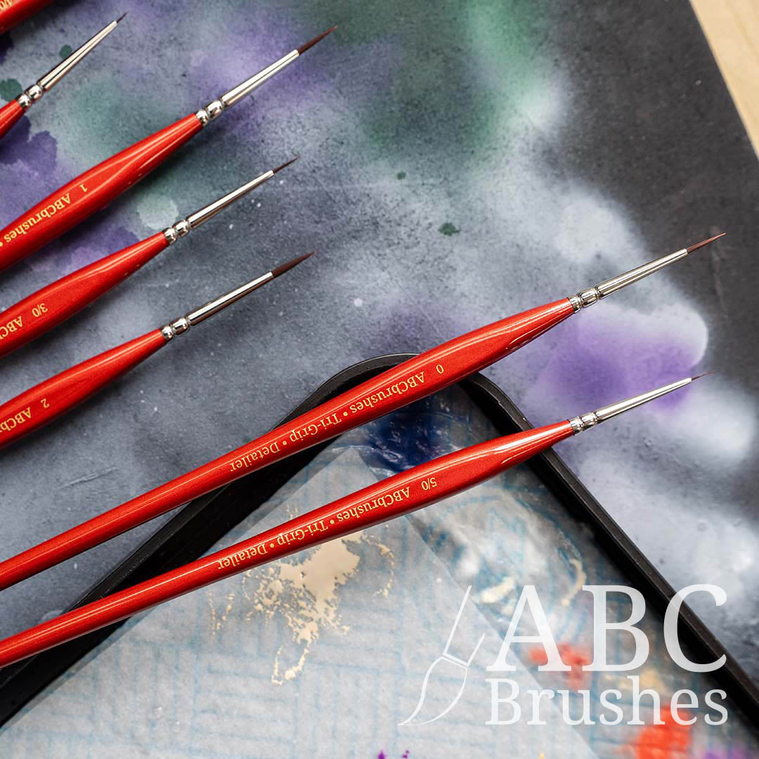 Close-up shot of the ABC Brushes Tri-Grip Detailer range on a paint covered cutting mat background and on to of a wet palette.