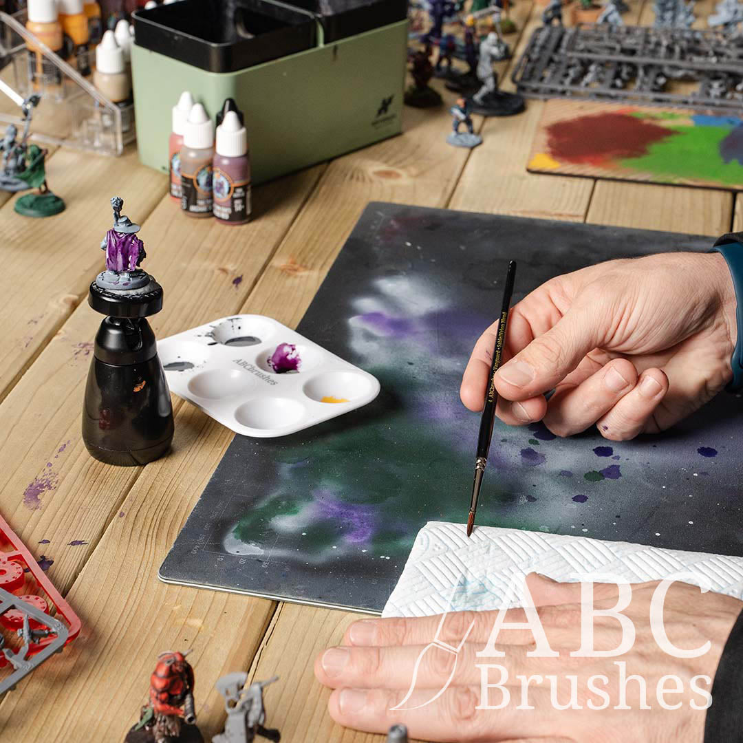 Wiping an ABC Brushes Vanguard paint brush on a paper towel, surrounded by various miniature figure painting supplies.