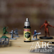 Bottle of the Army Painters Speedpaint in the colour Absolution Green, with wargaming models and an ABC paintbrush in the background, on a wooden surface.