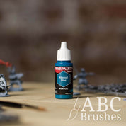 Bottle of the Army Painter Fanatics in the colour Abyssal Blue with various wargaming models and an ABC paintbrush in the background, on a wooden surface.
