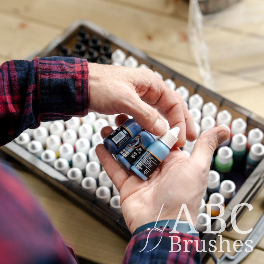 Selecting three bottles of blue acrylic paint from a box full of acrylic paint bottles.