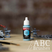 Bottle of the Army Painter Fanatics in the colour Aegis Aqua with various wargaming models and an ABC paintbrush in the background, on a wooden surface.