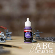 Bottle of the Army Painter Fanatics in the colour Alien Purple with various wargaming models and an ABC paintbrush in the background, on a wooden surface.