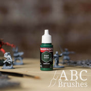 Bottle of the Army Painter Fanatics in the colour Angel Green with various wargaming models and an ABC paintbrush in the background, on a wooden surface.