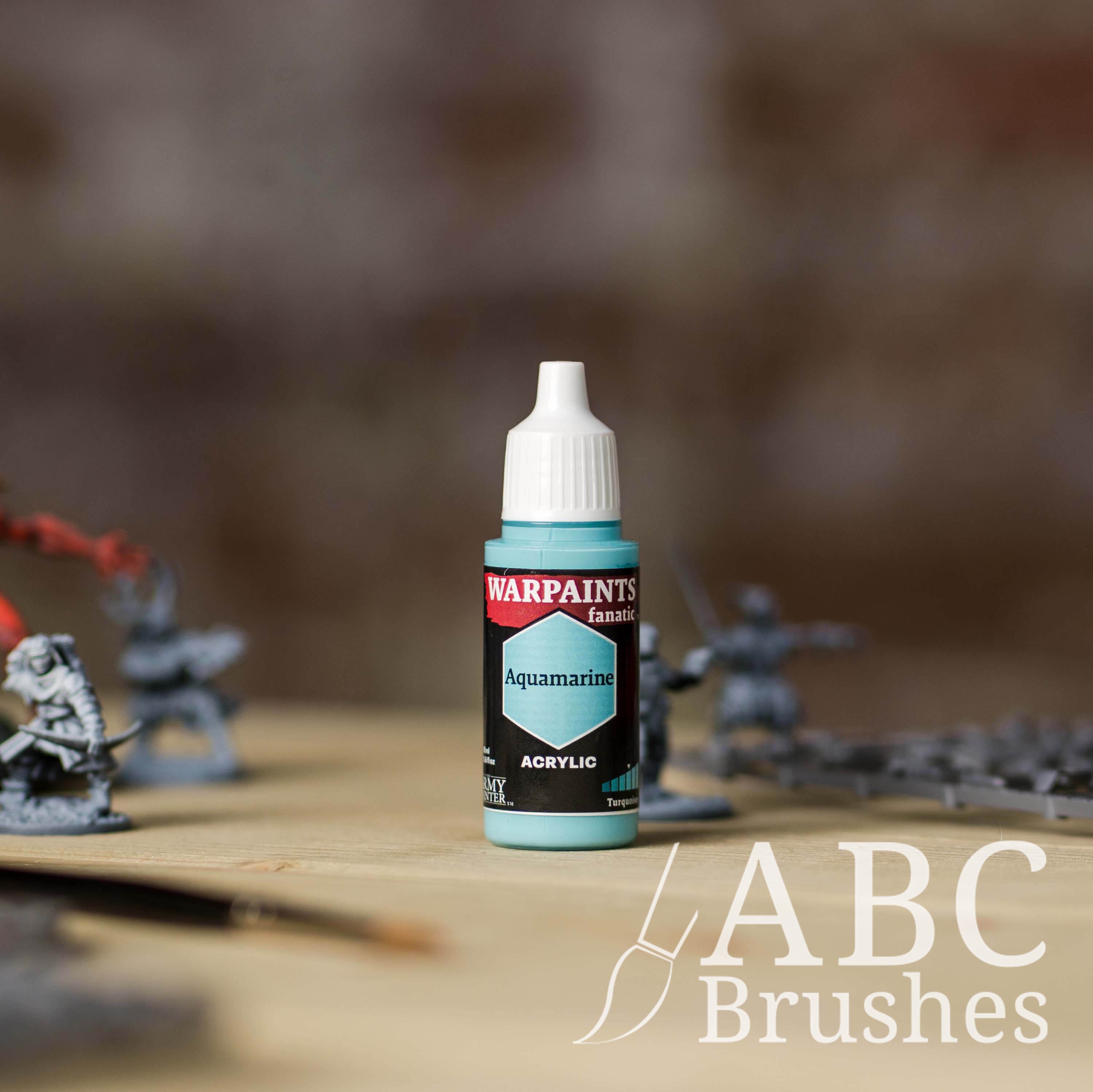 Bottle of the Army Painter Fanatics in the colour Aquamarine with various wargaming models and an ABC paintbrush in the background, on a wooden surface.
