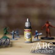 Bottle of the Army Painters Speedpaint in the colour Ashen Stone, with wargaming models and an ABC paintbrush in the background, on a wooden surface.