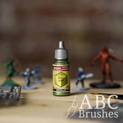 Bottle of the Army Painters Metallic Speedpaint in the colour Aztec Gold, with wargaming models and an ABC paintbrush in the background, on a wooden surface.
