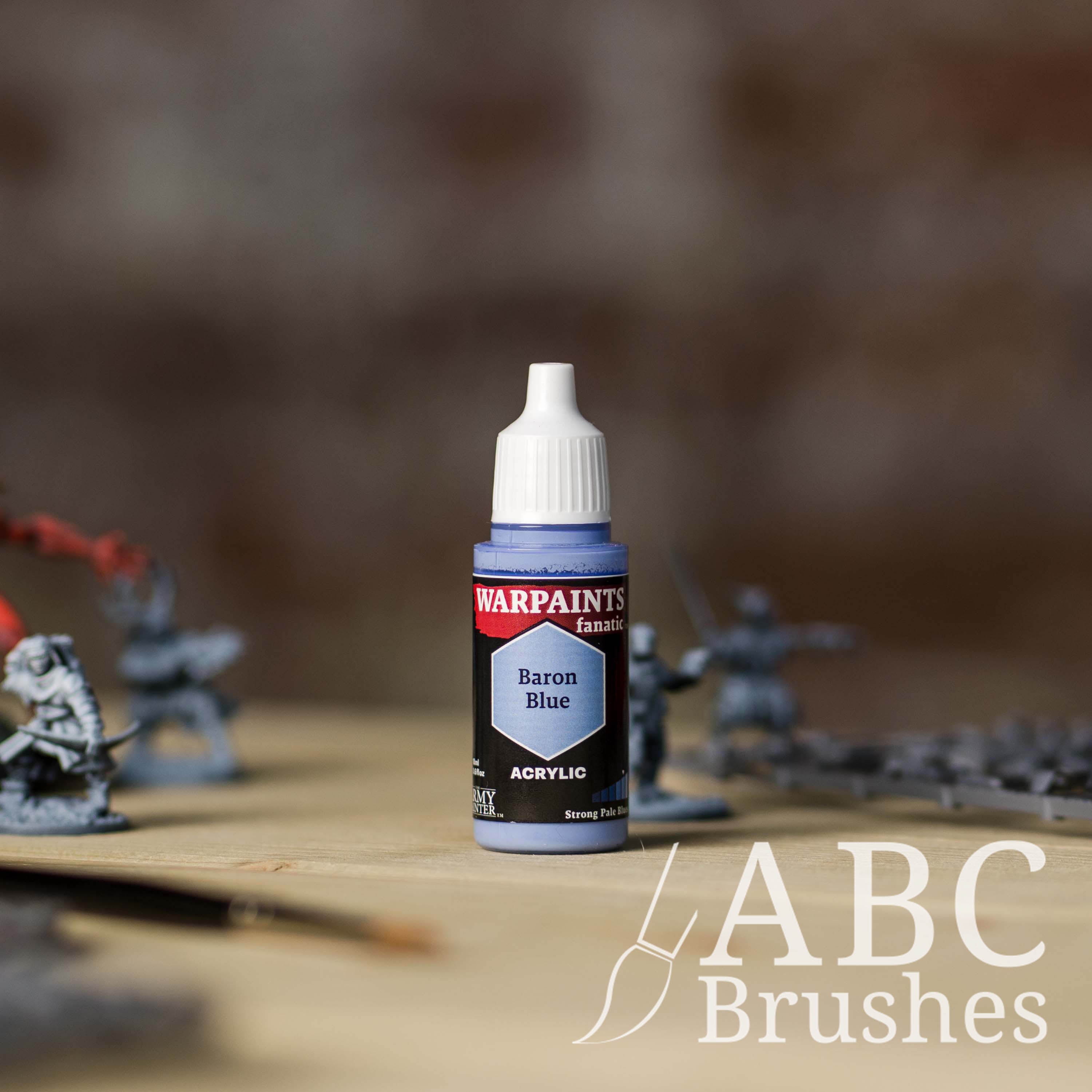 Bottle of the Army Painter Fanatics in the colour Baron Blue with various wargaming models and an ABC paintbrush in the background, on a wooden surface.