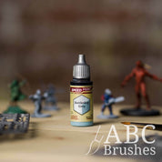 Bottle of the Army Painters Speedpaint in the colour Battleship Grey, with wargaming models and an ABC paintbrush in the background, on a wooden surface.