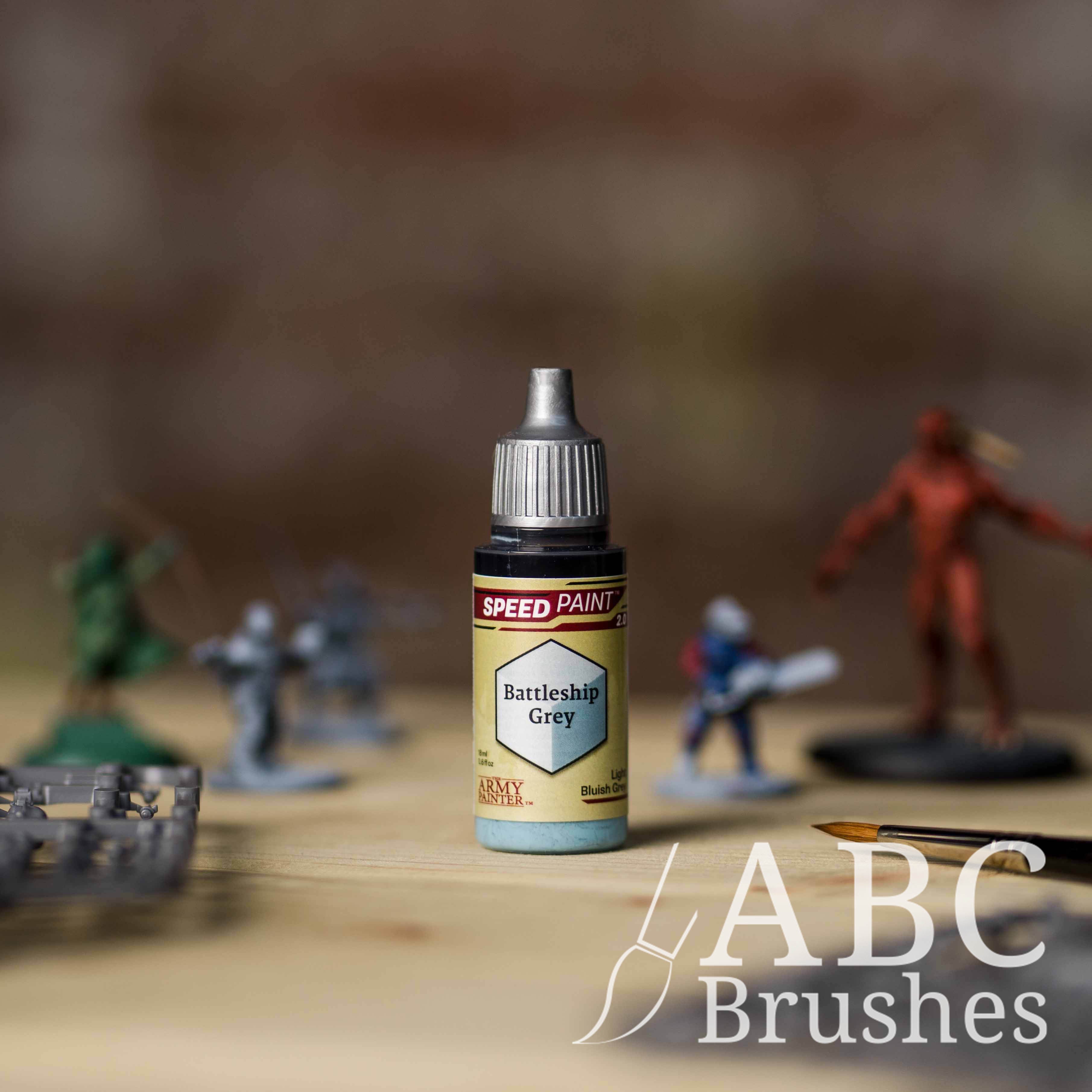 Bottle of the Army Painters Speedpaint in the colour Battleship Grey, with wargaming models and an ABC paintbrush in the background, on a wooden surface.