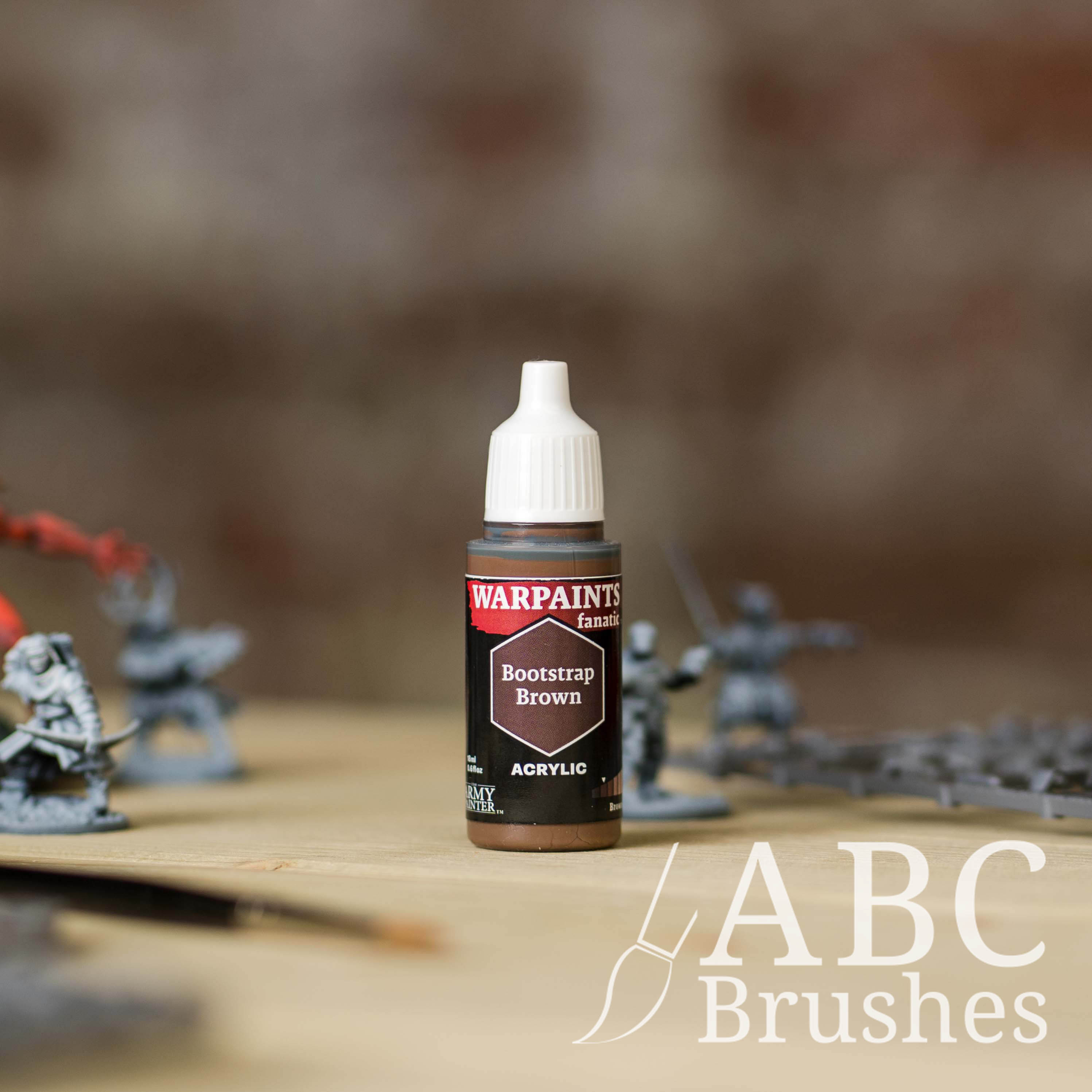 Bottle of the Army Painter Fanatics in the colour Bootstrap Brown with various wargaming models and an ABC paintbrush in the background, on a wooden surface.