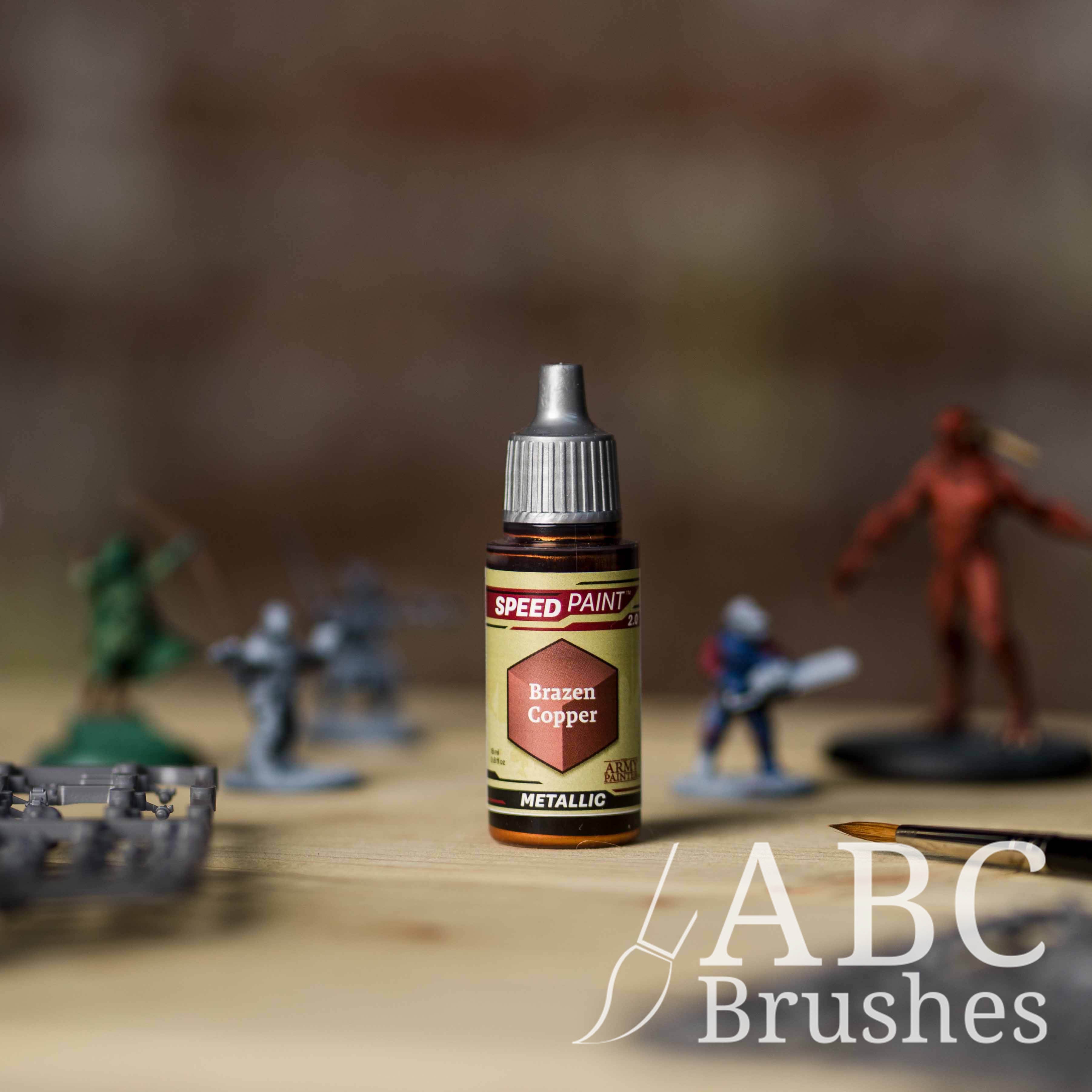 Bottle of the Army Painters Metallic Speedpaint in the colour Brazen Copper, with wargaming models and an ABC paintbrush in the background, on a wooden surface.