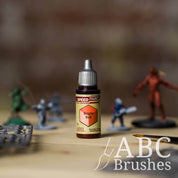 Bottle of the Army Painters Speedpaint in the colour Bright Red, with wargaming models and an ABC paintbrush in the background, on a wooden surface.