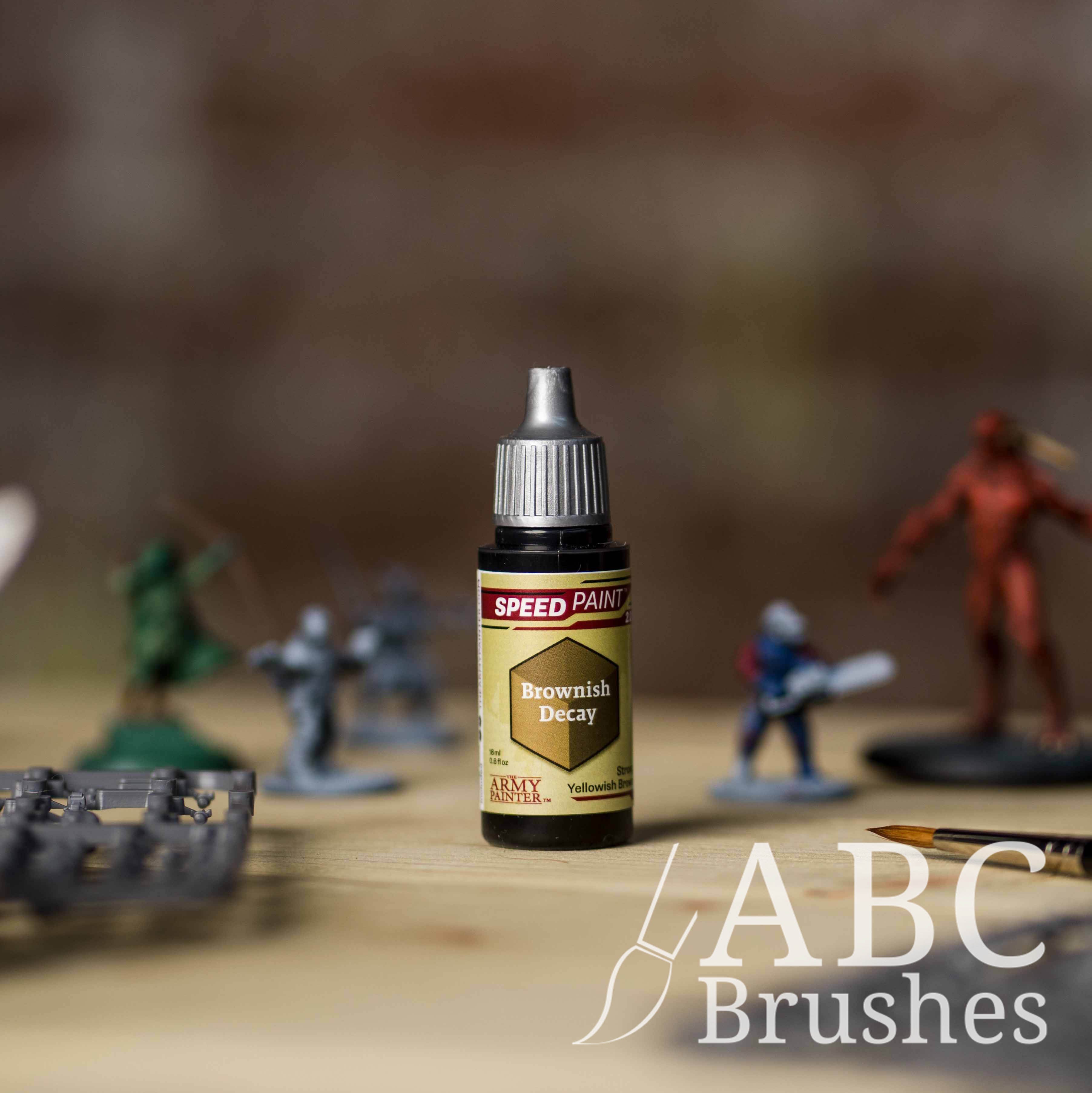 Bottle of the Army Painters Speedpaint in the colour Brownish Decay, with wargaming models and an ABC paintbrush in the background, on a wooden surface.