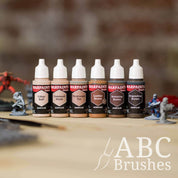 Army Painter Fanatics Browns Triad on a wooden surface. There are wargaming models and an ABC paint brush next to them.