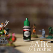 Bottle of the Army Painter Fanatics Effects Grey Brush-on Primer with various wargaming models and an ABC paintbrush in the background, on a wooden surface.