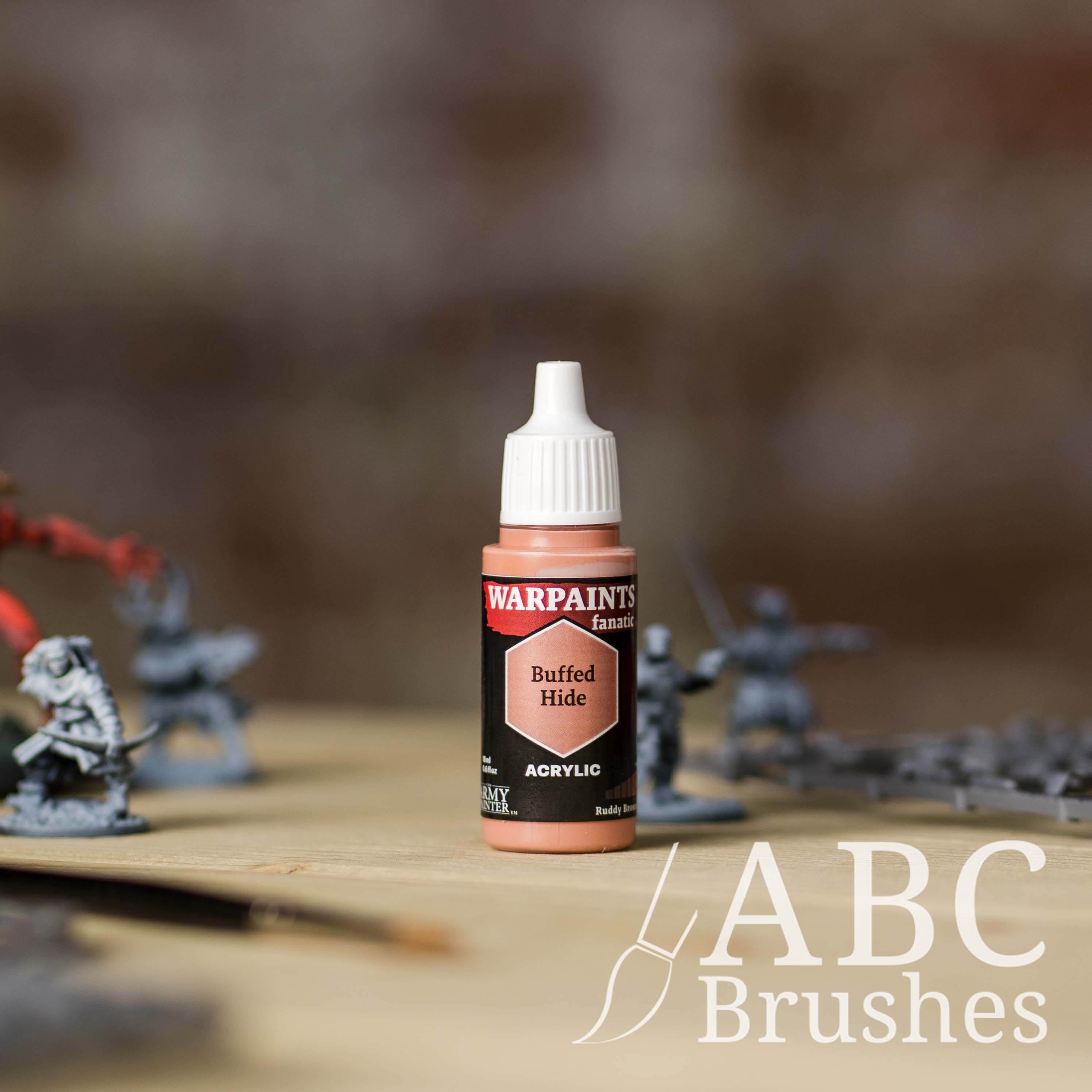 Bottle of the Army Painter Fanatics in the colour Buffed Hide with various wargaming models and an ABC paintbrush in the background, on a wooden surface.
