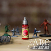 Bottle of the Army Painters Speedpaint in the colour Carmine Dragon, with wargaming models and an ABC paintbrush in the background, on a wooden surface.