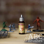 Bottle of the Army Painters Speedpaint in the colour Crusader Skin, with wargaming models and an ABC paintbrush in the background, on a wooden surface.