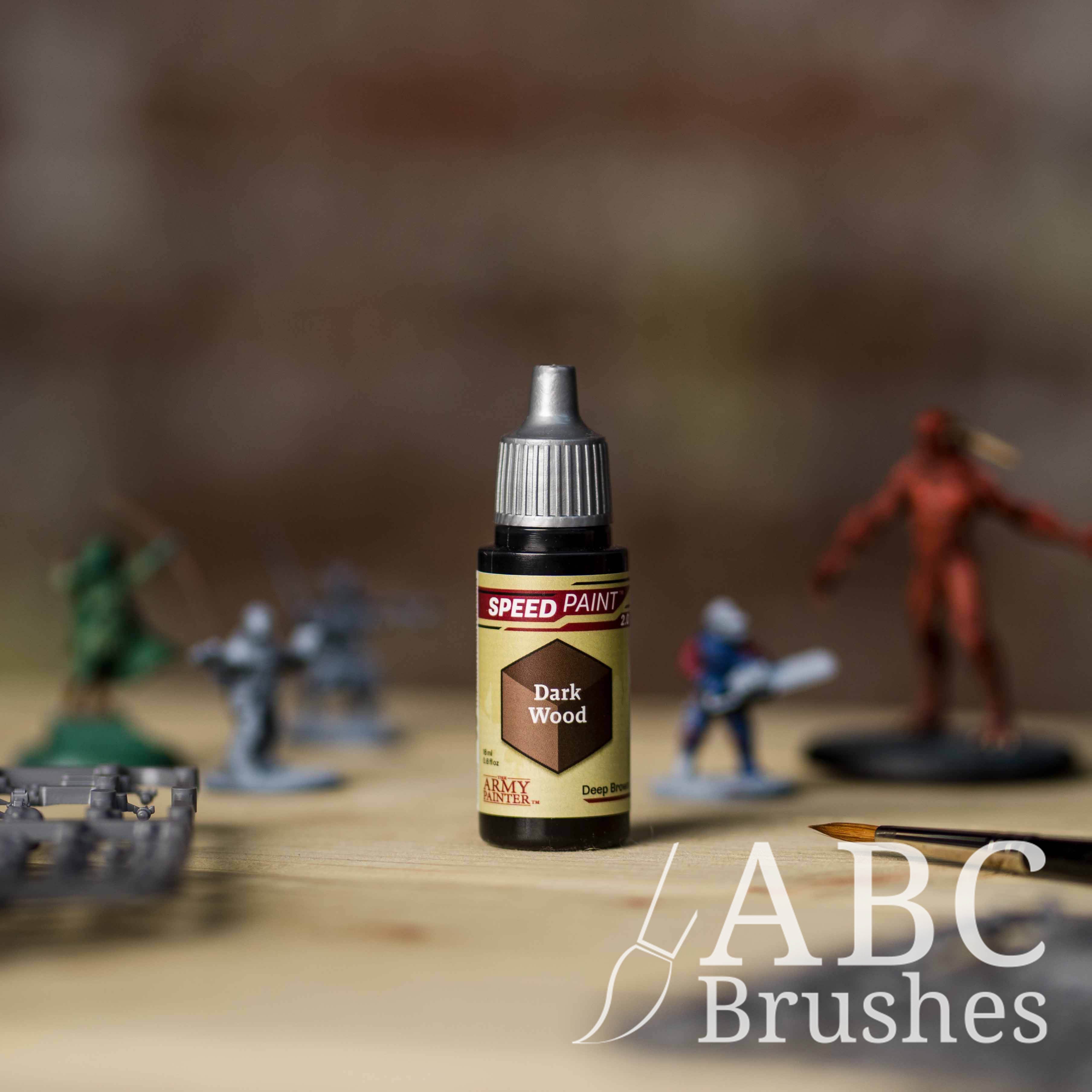 Bottle of the Army Painters Speedpaint in the colour Dark Wood, with wargaming models and an ABC paintbrush in the background, on a wooden surface.