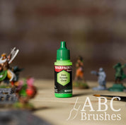 Bottle of the Army Painter Fanatics Effects in the colour Data System Glow with various wargaming models and an ABC paintbrush in the background, on a wooden surface.