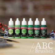 Army Painter Fanatics Deep Greens Triad on a wooden surface. There are wargaming models and an ABC paint brush next to them.