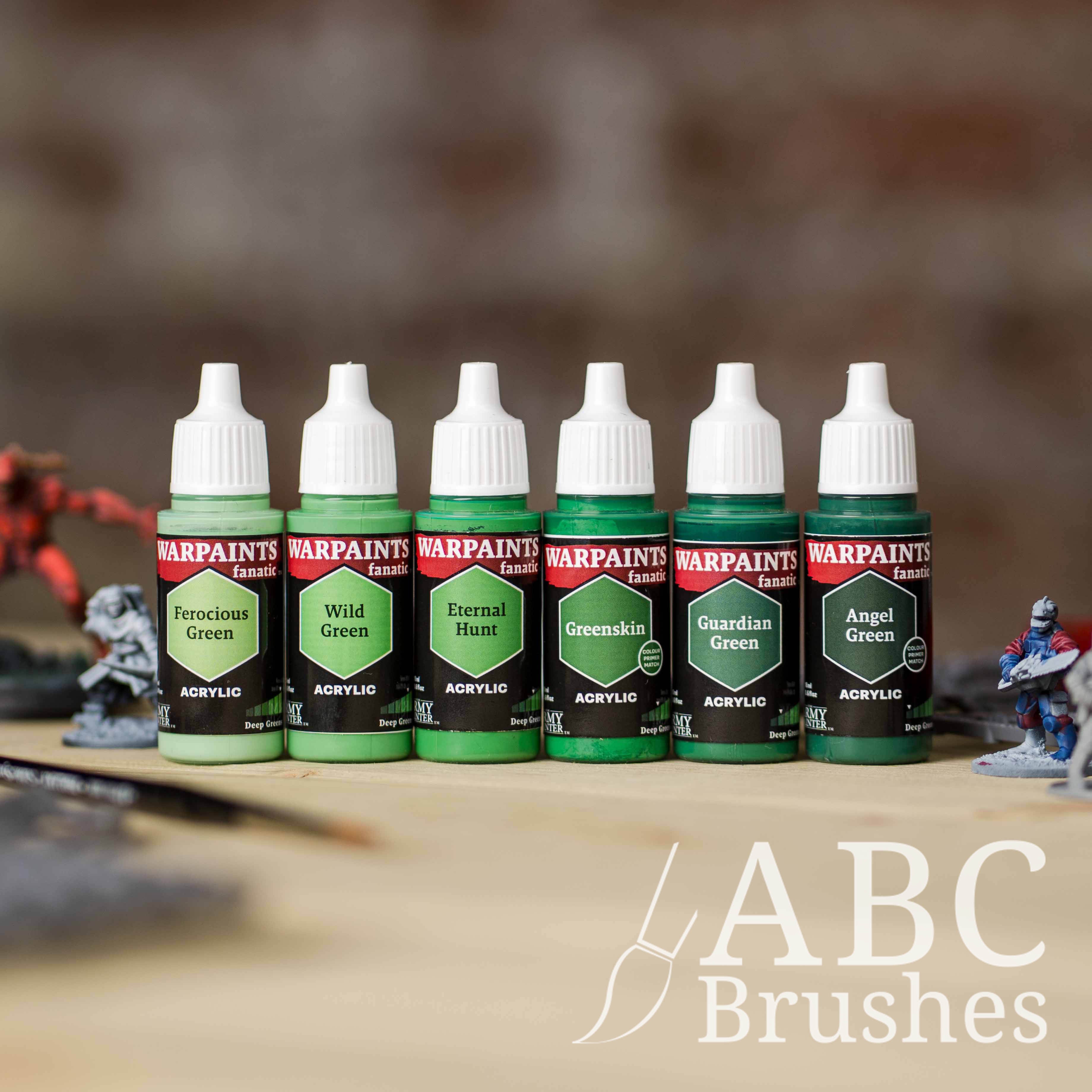 Army Painter Fanatics Deep Greens Triad on a wooden surface. There are wargaming models and an ABC paint brush next to them.