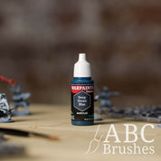 Bottle of the Army Painter Fanatics in the colour Deep Ocean Blue with various wargaming models and an ABC paintbrush in the background, on a wooden surface.