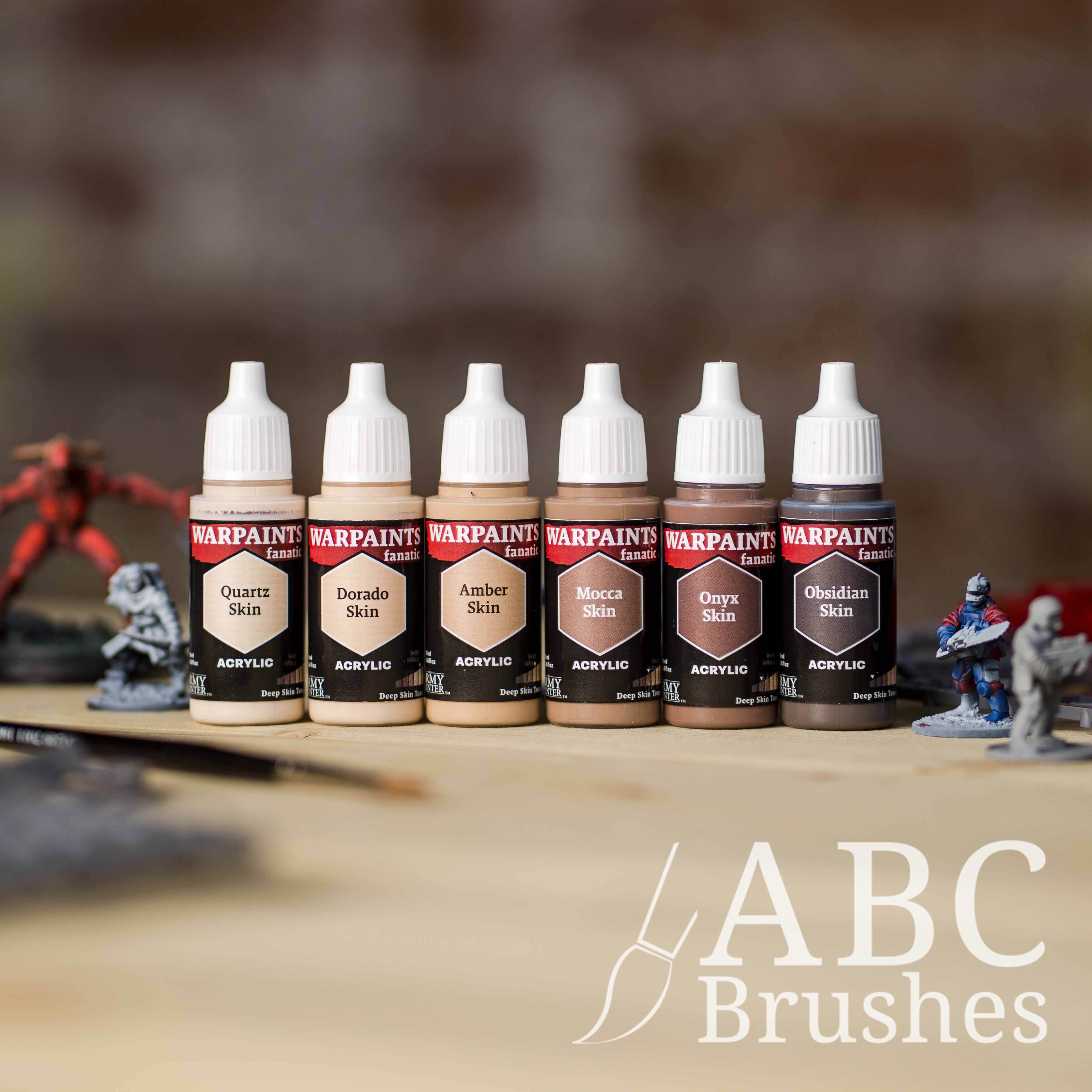 Army Painter Fanatics Deep Skin Tone Triad on a wooden surface. There are wargaming models and an ABC paint brush next to them.