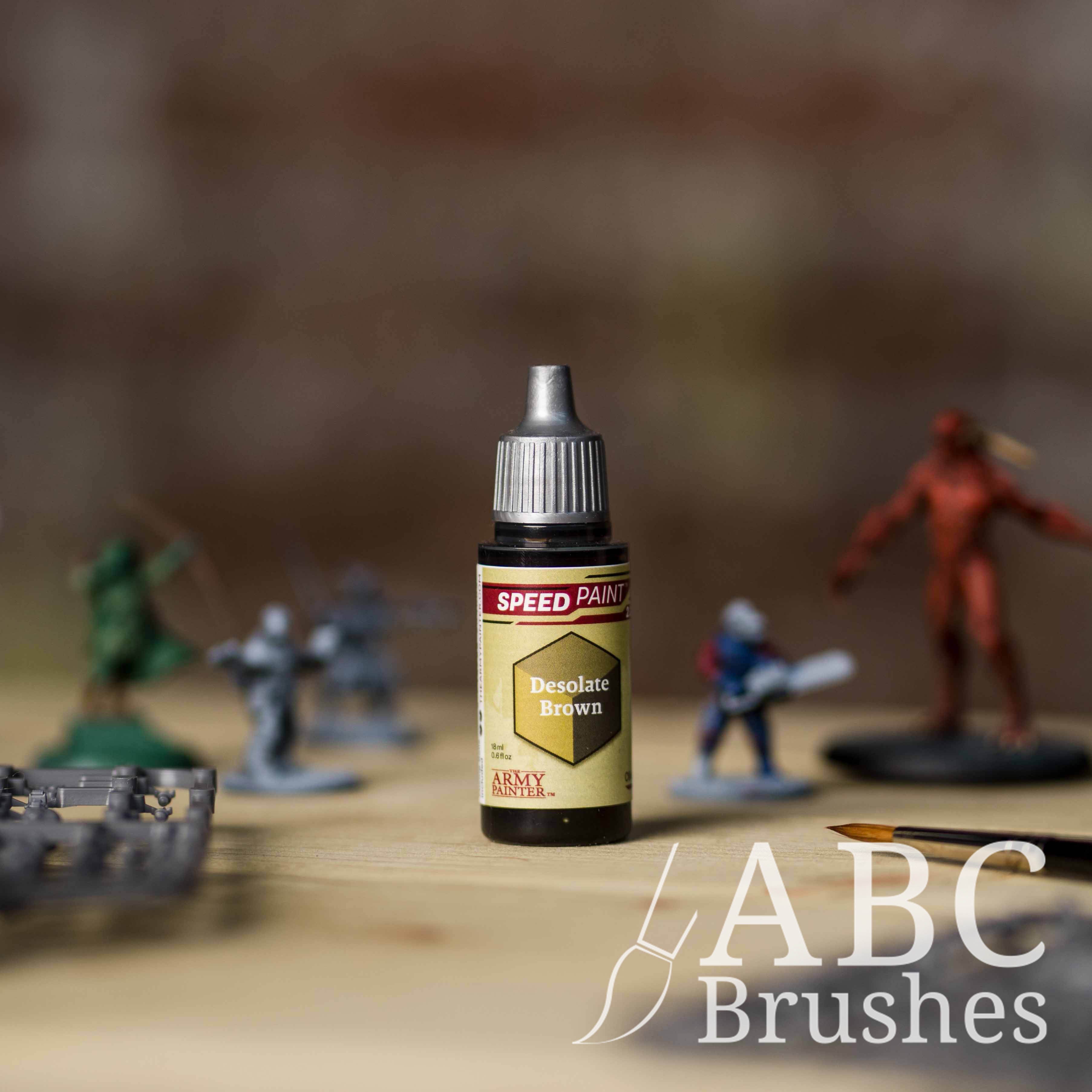 Bottle of the Army Painters Speedpaint in the colour Desolate Brown, with wargaming models and an ABC paintbrush in the background, on a wooden surface.
