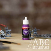 Bottle of the Army Painter Fanatics in the colour Diabolic Plum with various wargaming models and an ABC paintbrush in the background, on a wooden surface.