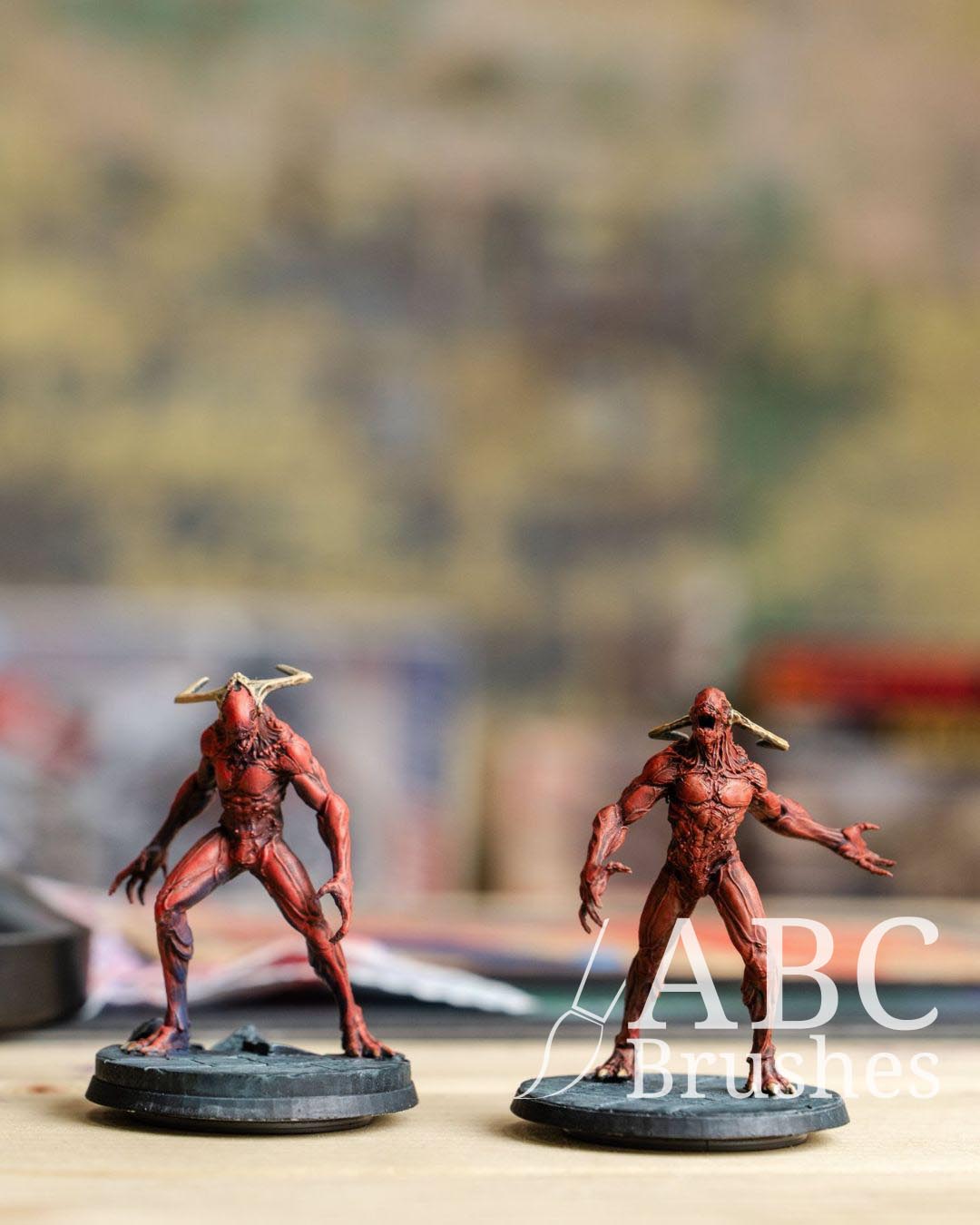 Two red demon miniatures, painted in red with a darker dry brush effect over their bodies. Their horn are yellow and the base of the models is blue-grey colour. 