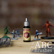 Bottle of the Army Painters Speedpaint in the colour Dusk Red, with wargaming models and an ABC paintbrush in the background, on a wooden surface.