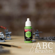 Bottle of the Army Painter Fanatics in the colour Emerald Forest with various wargaming models and an ABC paintbrush in the background, on a wooden surface.