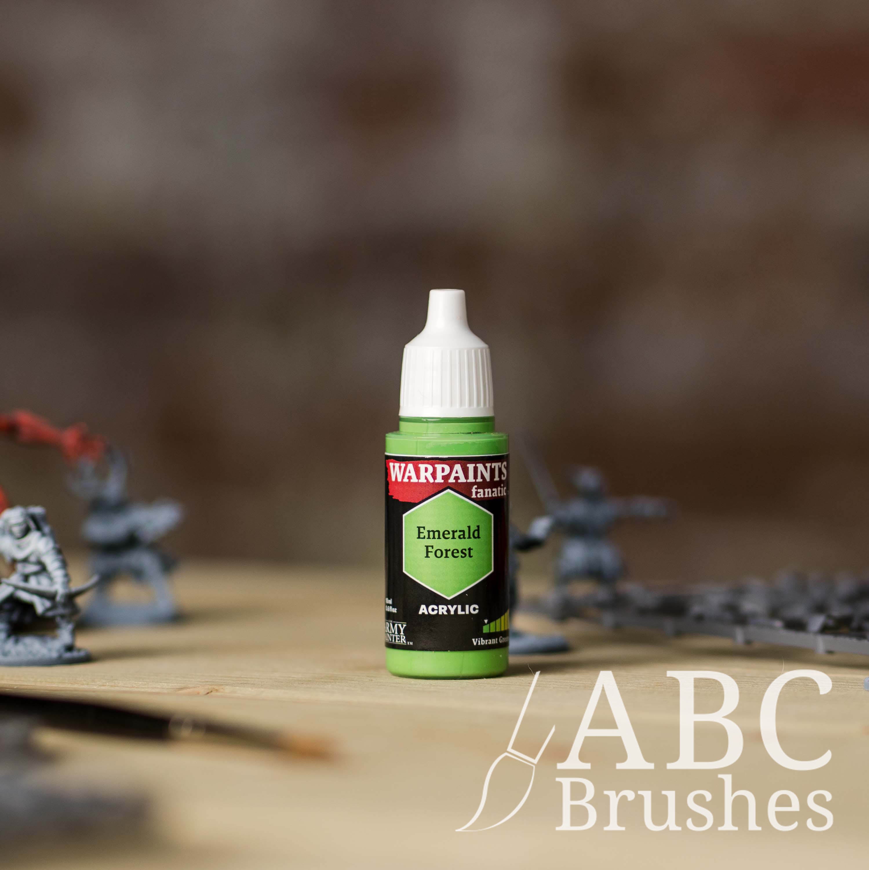 Bottle of the Army Painter Fanatics in the colour Emerald Forest with various wargaming models and an ABC paintbrush in the background, on a wooden surface.
