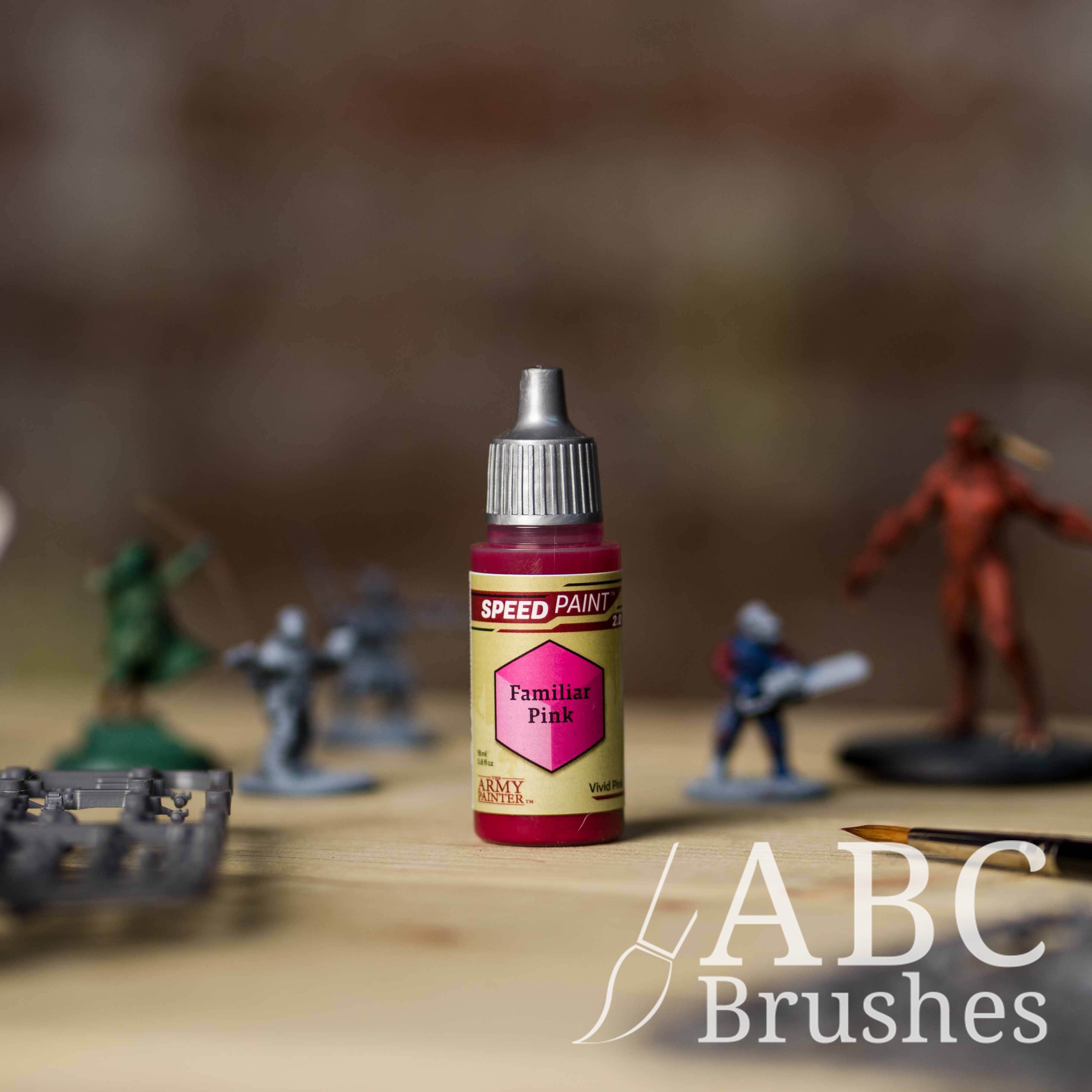 Bottle of the Army Painters Speedpaint in the colour Familiar Pink, with wargaming models and an ABC paintbrush in the background, on a wooden surface.