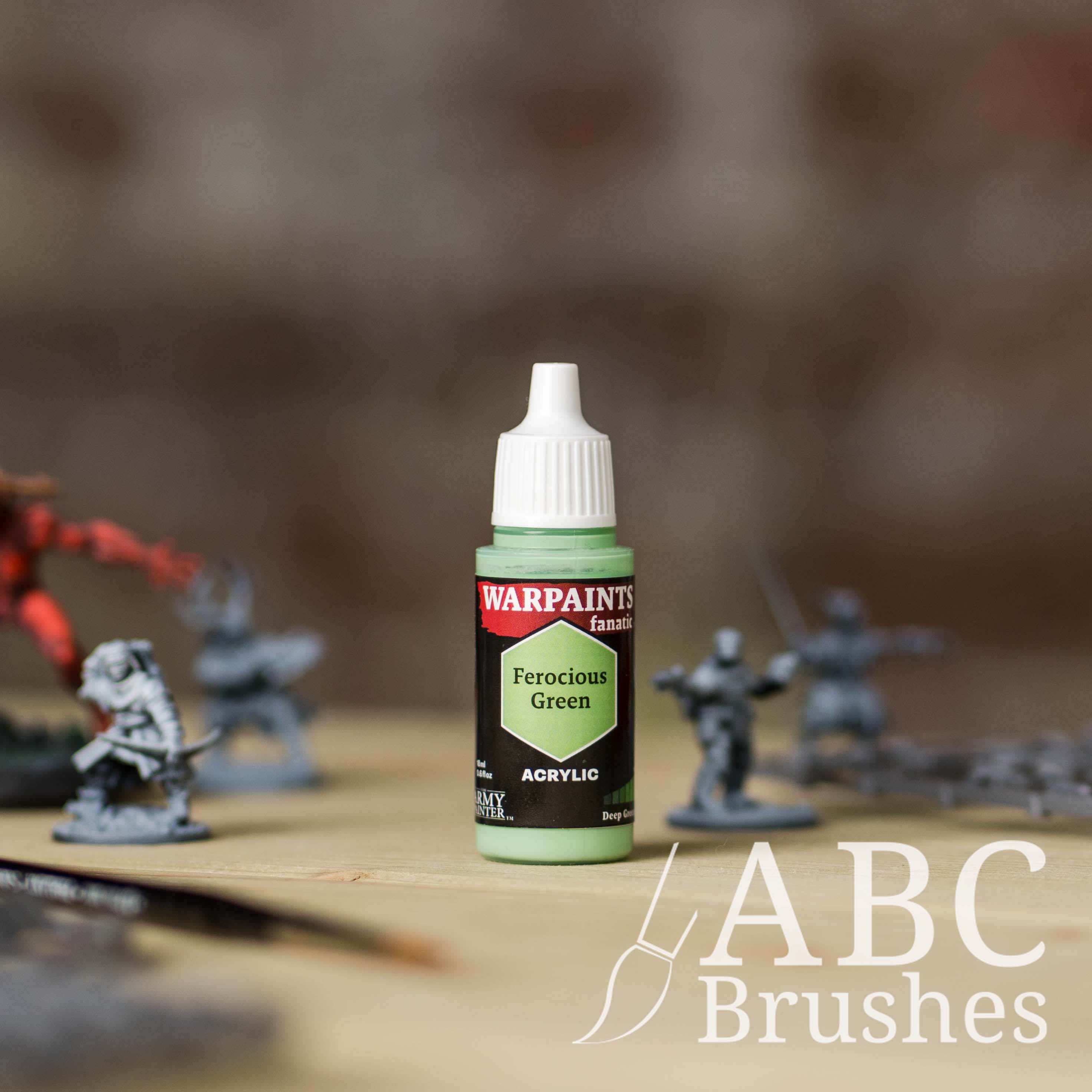 Bottle of the Army Painter Fanatics in the colour Ferocious Green with various wargaming models and an ABC paintbrush in the background, on a wooden surface.