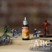 Bottle of the Army Painters Speedpaint in the colour Fire Giant Orange, with wargaming models and an ABC paintbrush in the background, on a wooden surface.