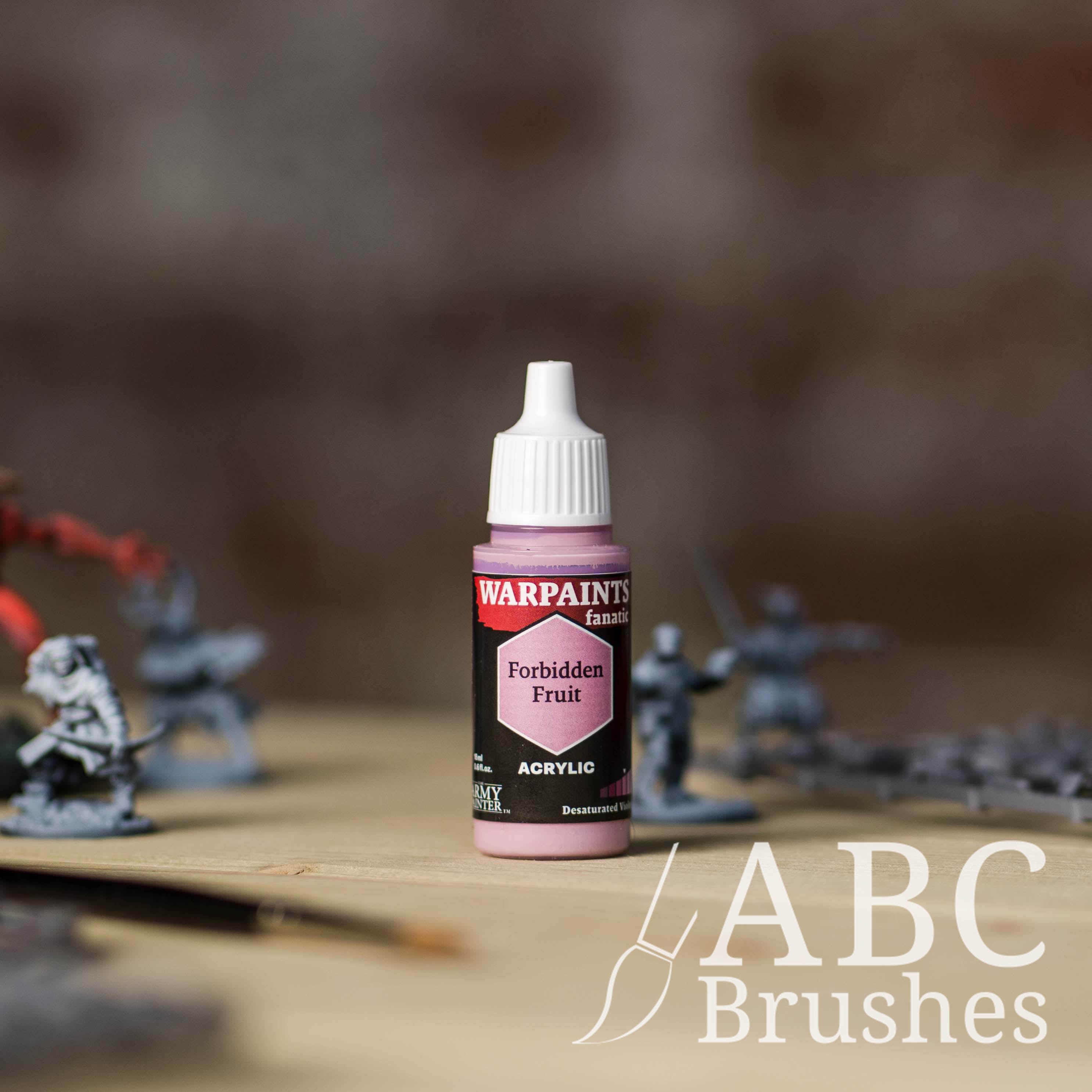 Bottle of the Army Painter Fanatics in the colour Forbidden Fruit with various wargaming models and an ABC paintbrush in the background, on a wooden surface.