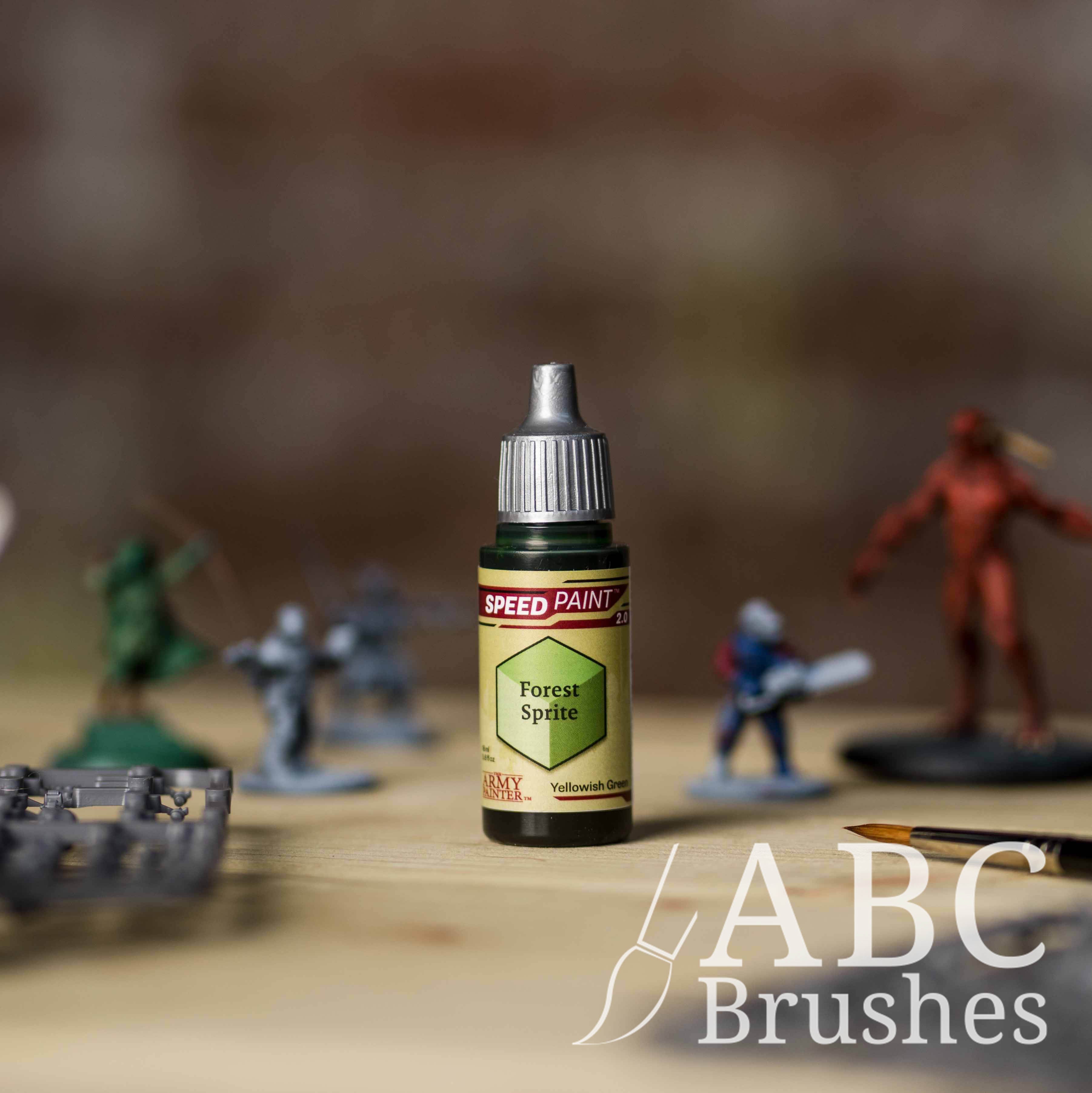 Bottle of the Army Painters Speedpaint in the colour Forest Sprite, with wargaming models and an ABC paintbrush in the background, on a wooden surface.