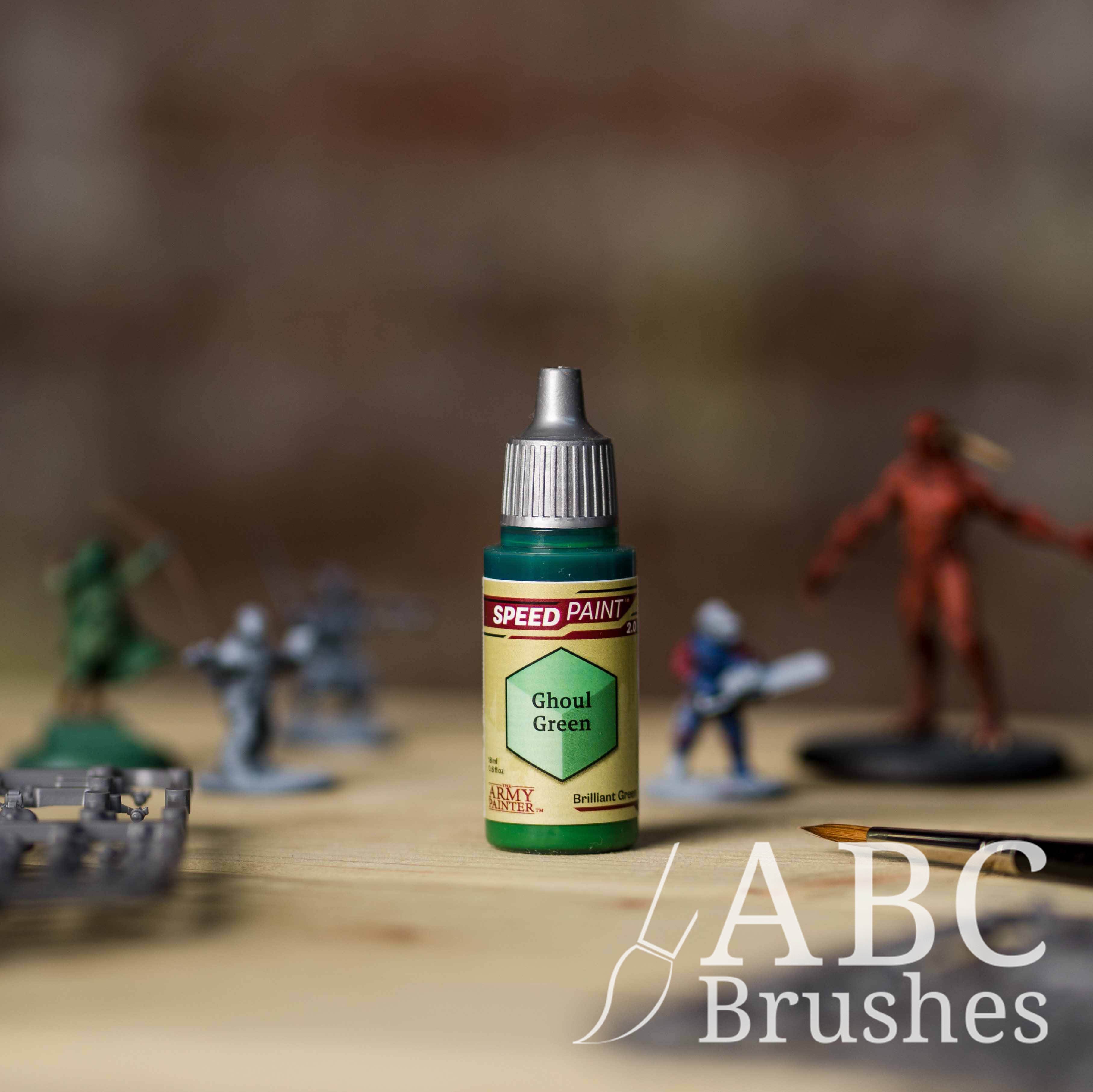 Bottle of the Army Painters Speedpaint in the colour Ghoul Green, with wargaming models and an ABC paintbrush in the background, on a wooden surface.