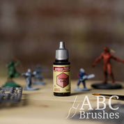 Bottle of the Army Painters Speedpaint in the colour Goddess Glow, with wargaming models and an ABC paintbrush in the background, on a wooden surface.