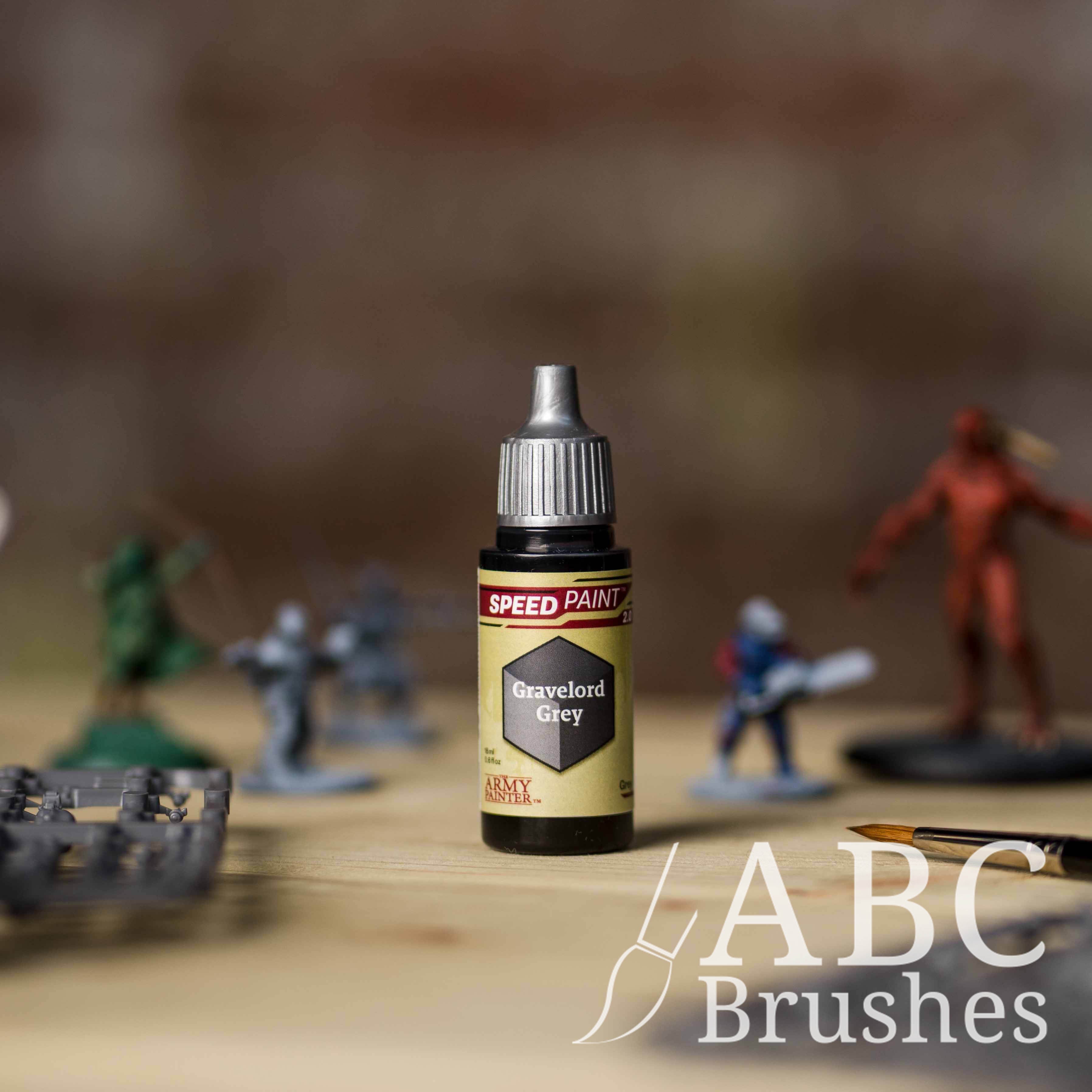 Bottle of the Army Painters Speedpaint in the colour Gravelord Grey, with wargaming models and an ABC paintbrush in the background, on a wooden surface.