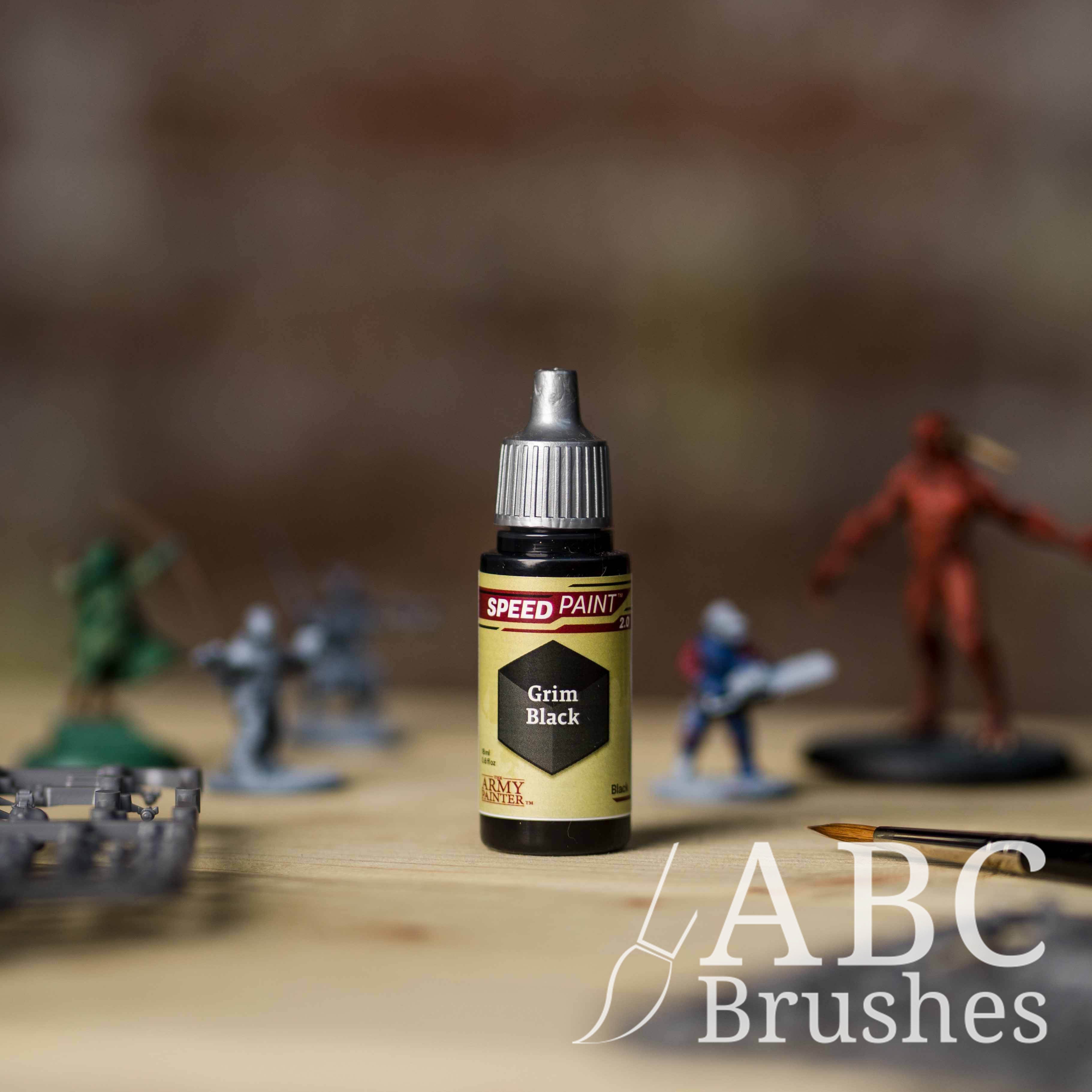 Bottle of the Army Painters Speedpaint in the colour Grim Black, with wargaming models and an ABC paintbrush in the background, on a wooden surface.