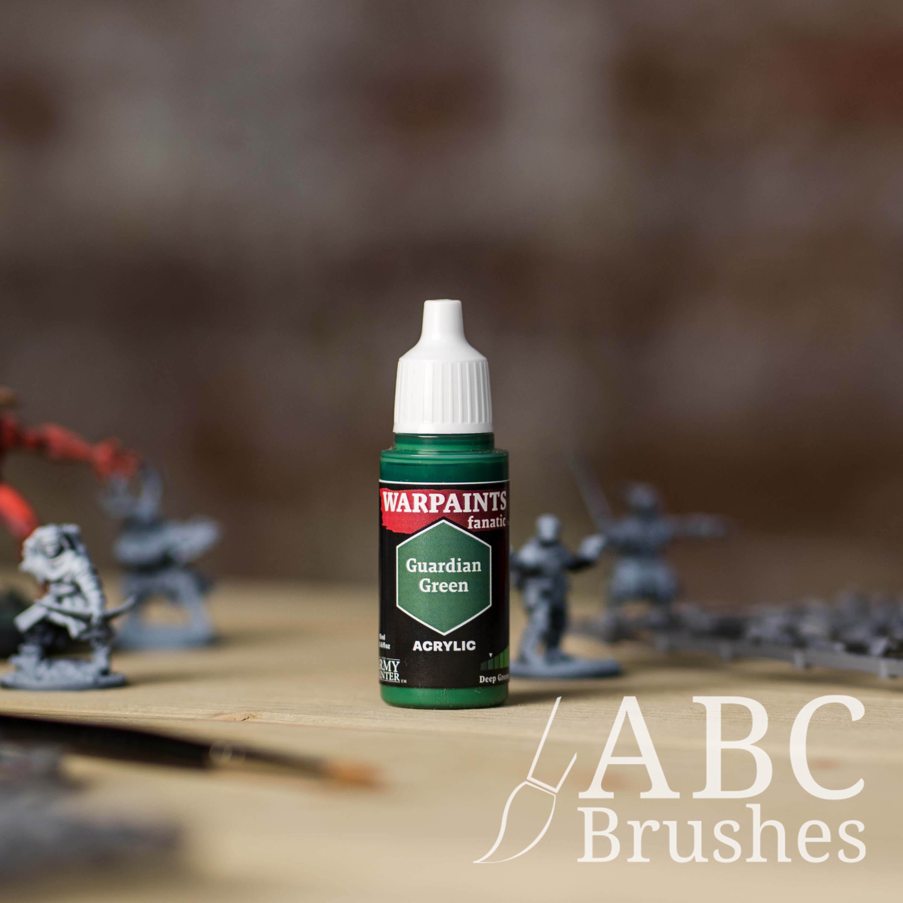 Bottle of the Army Painter Fanatics in the colour Guardian Green with various wargaming models and an ABC paintbrush in the background, on a wooden surface.