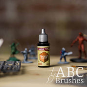 Bottle of the Army Painters Speedpaint in the colour Hardened Leather, with wargaming models and an ABC paintbrush in the background, on a wooden surface.