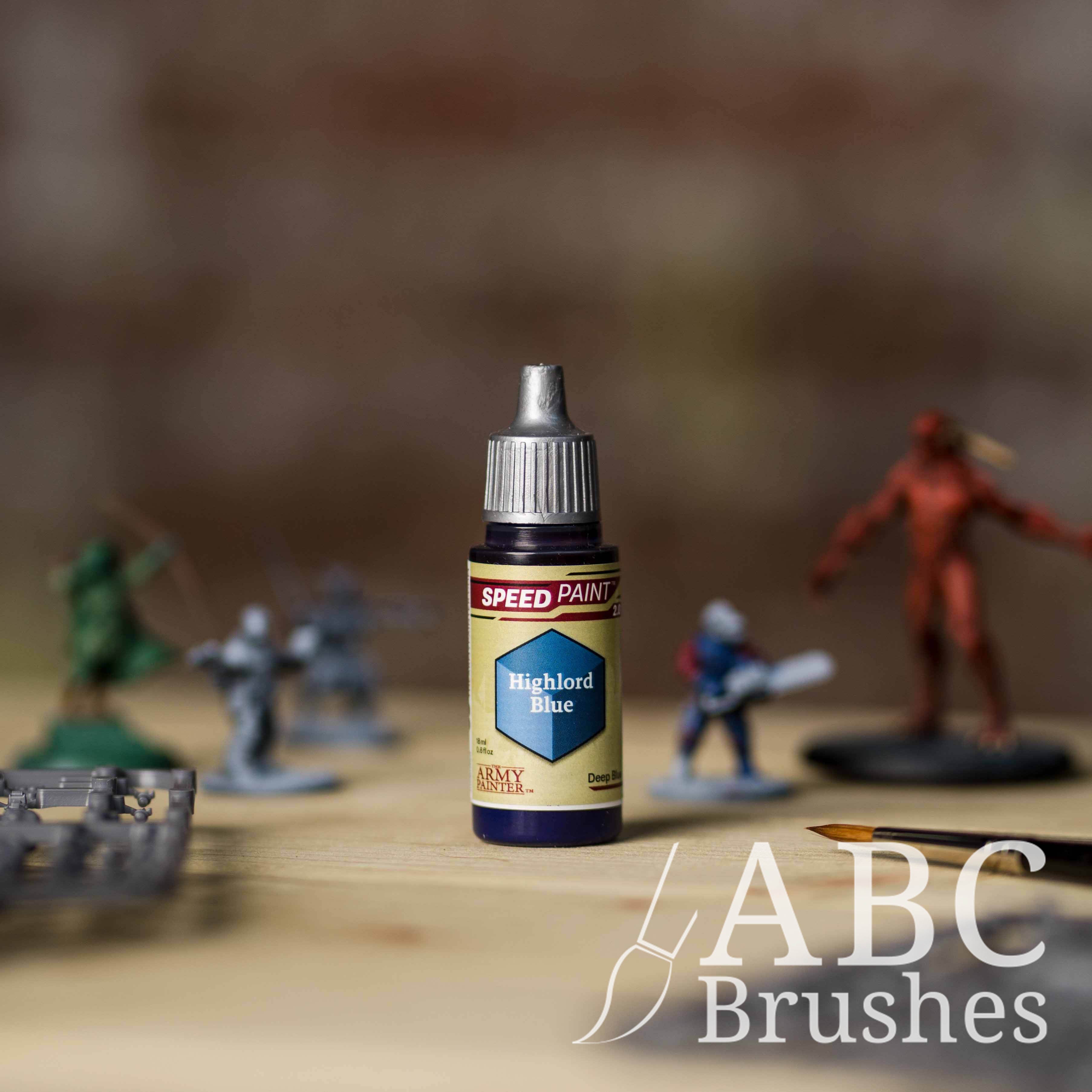 Bottle of the Army Painters Speedpaint in the colour Highlord Blue, with wargaming models and an ABC paintbrush in the background, on a wooden surface.